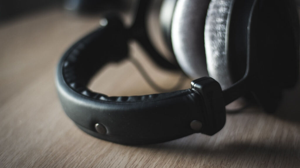 A pair of over-ear studio headphones resting on a wooden desk, the headband in focus.