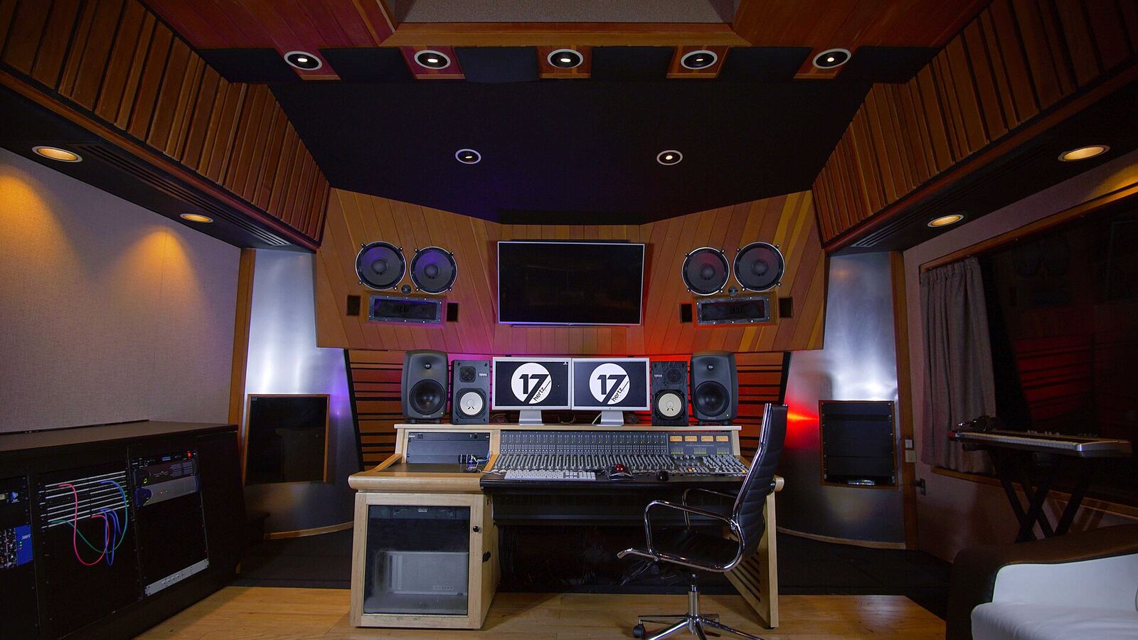 A professional control room with wood-slat diffusers, angled wall treatment and a mixing desk between the monitors.