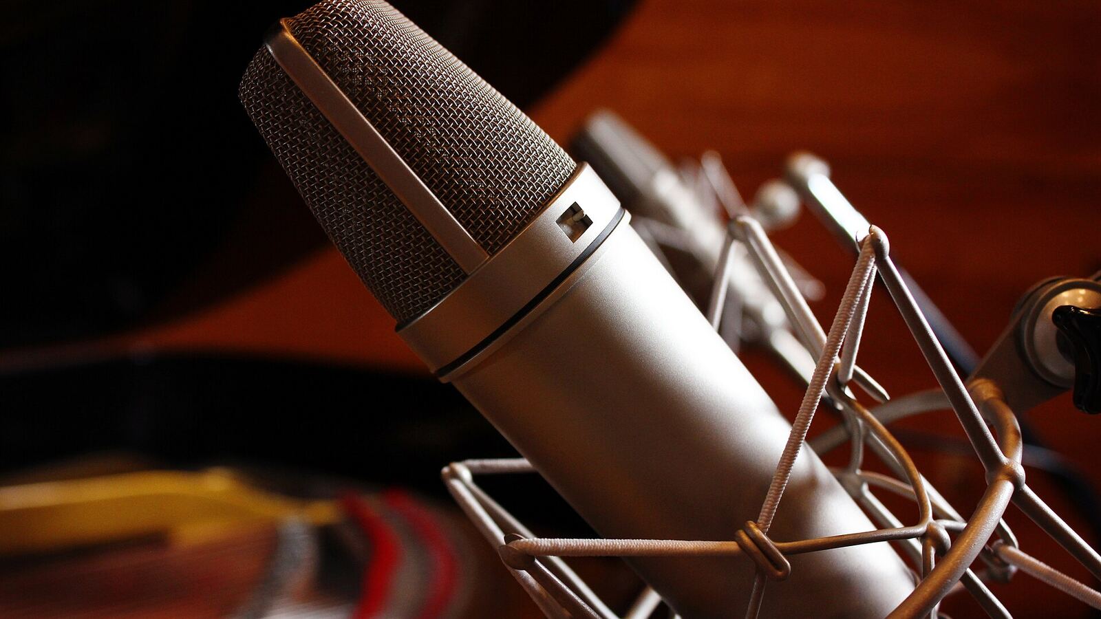 A large-diaphragm condenser microphone in a shock mount, photographed close up in a recording studio.