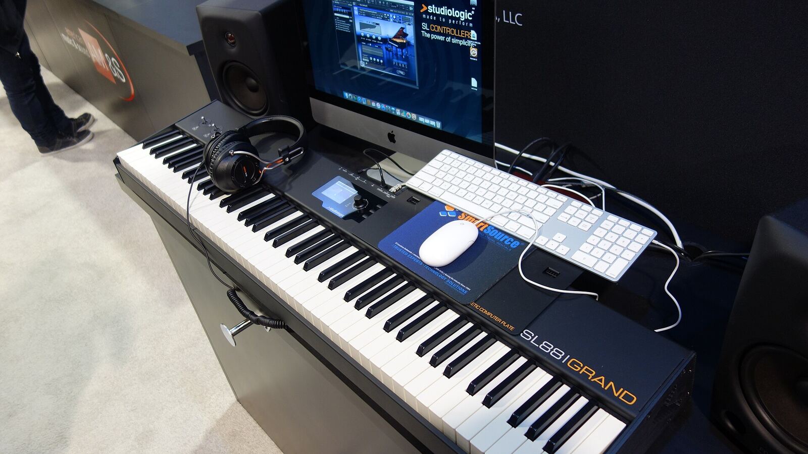A full-size 88-key MIDI keyboard controller set up in front of a computer, monitors and a computer keyboard.