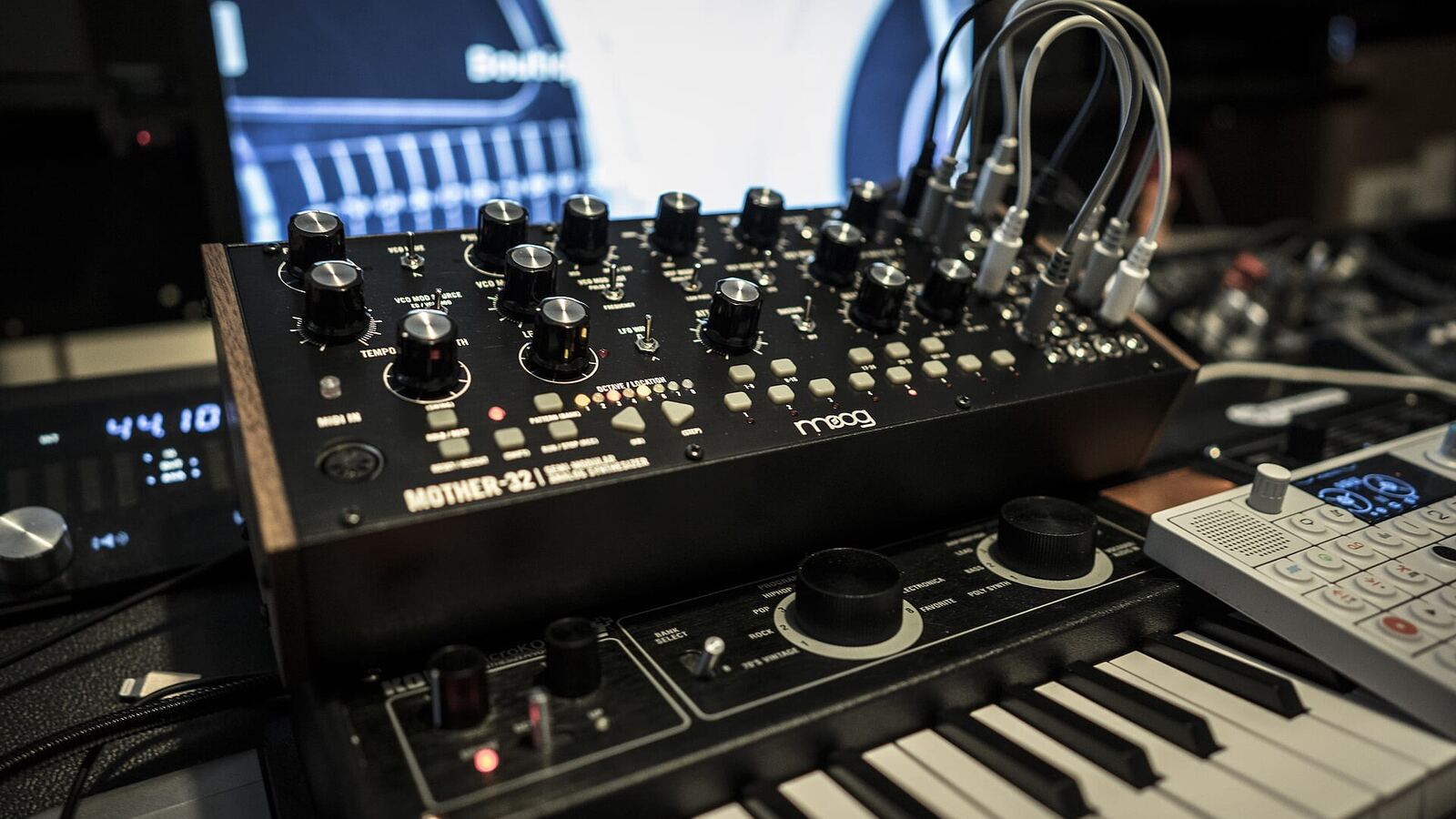 A semi-modular analog synthesizer covered in knobs and patch cables, sitting above a small keyboard.